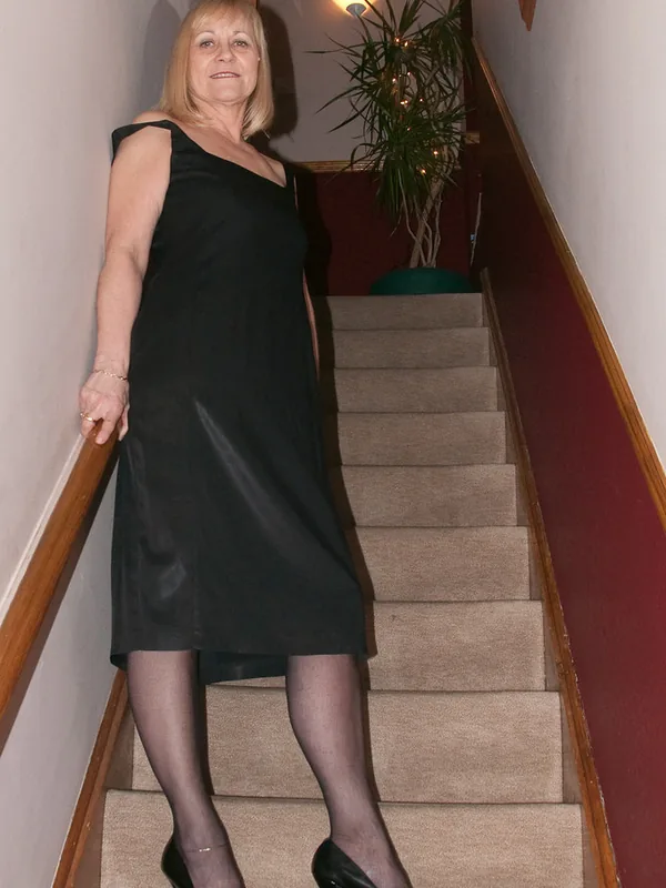 Personne en robe noire descendant un escalier, main sur la rampe, plante en arrière-plan