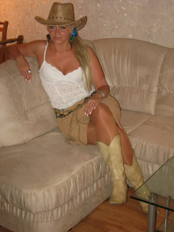 Personne en tenue cowgirl, chapeau, bottes, jupe courte, assise sur canapé beige