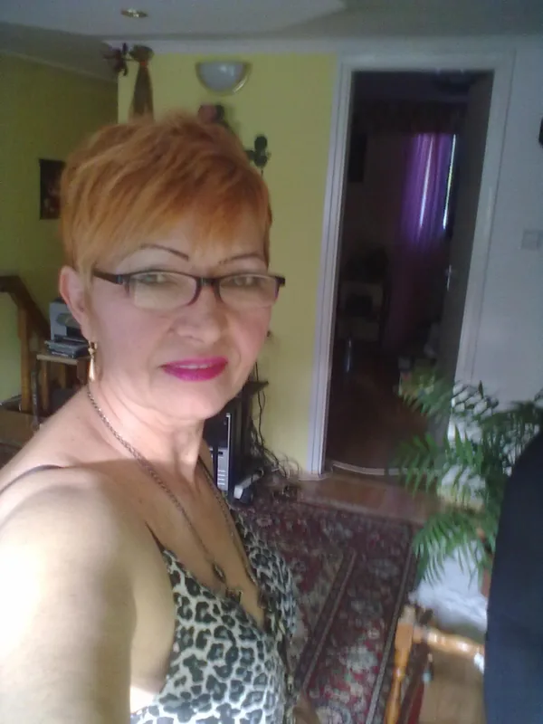 Portrait de personne aux cheveux courts roux, lunettes, maquillage, haut léopard, intérieur maison