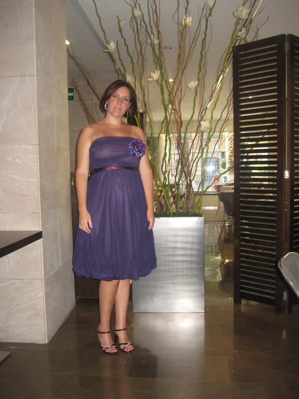 Personne en robe violette posant devant une installation florale dans un hall intérieur