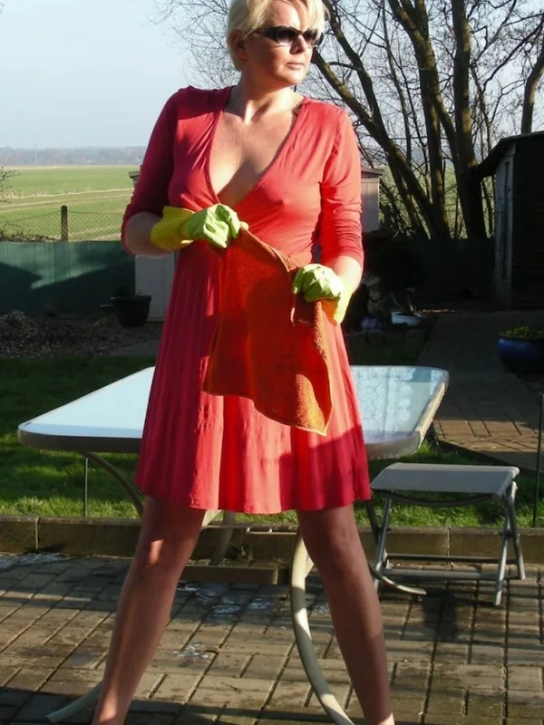 Personne en robe rouge et gants de jardinage, tenant un chiffon, sur une terrasse ensoleillée