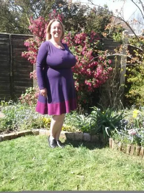 Personne souriante en robe violette dans un jardin fleuri ensoleillé