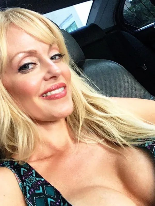 Portrait d'une personne blonde souriante dans une voiture, portant un haut à motifs colorés
