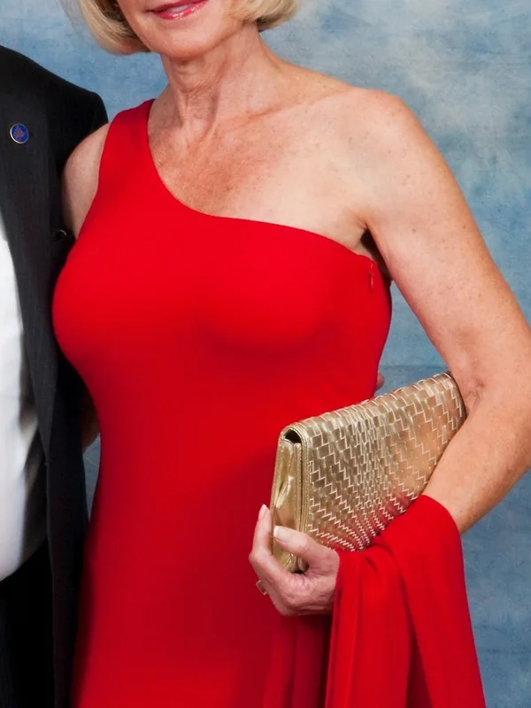 Personne en robe rouge asymétrique tenant un sac doré, devant fond bleu texturé